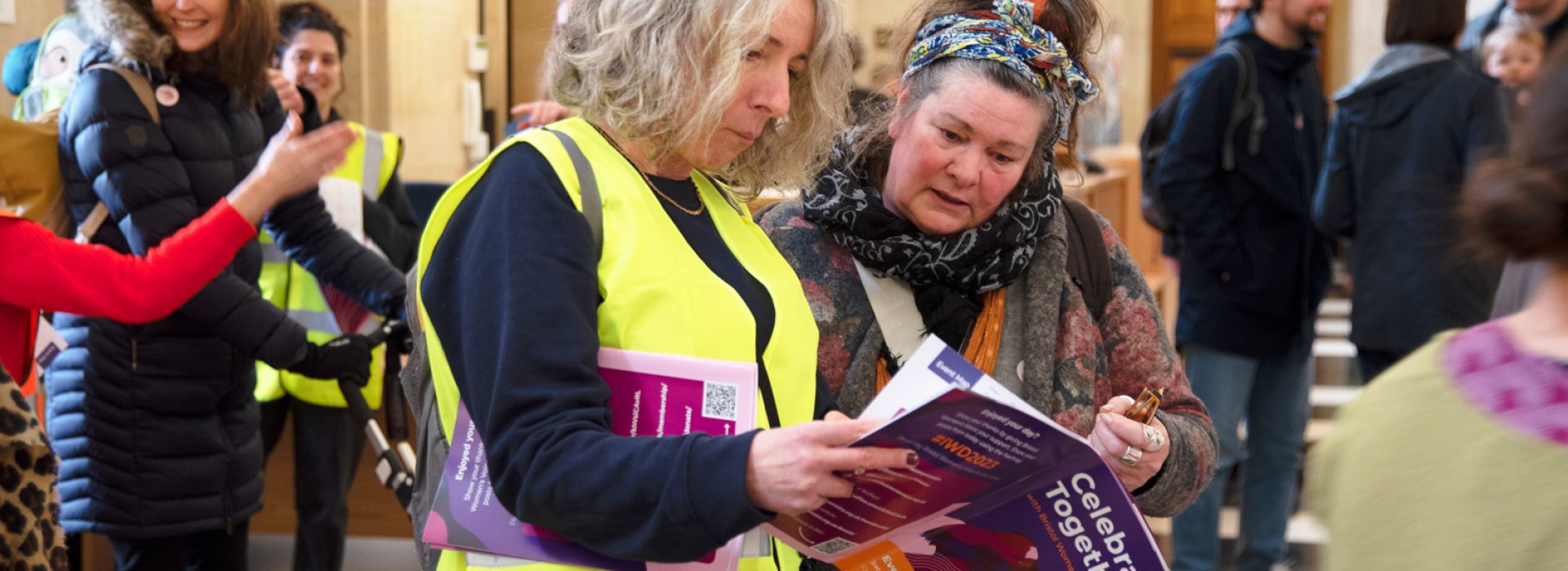 Two women standing in city hall and viewing a copy of International Women's Day programme