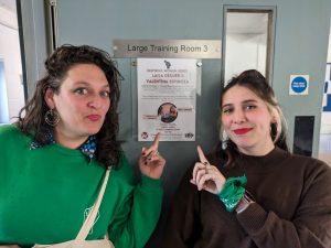 Two women pointing at a poster